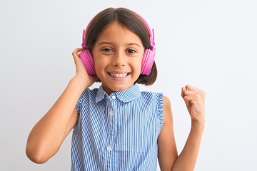 Beautiful child girl listening to music using headphones over isolated white background screaming proud and celebrating victory and success very excited, cheering emotion