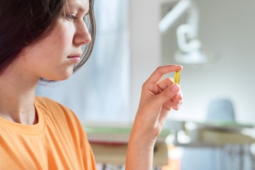 Wall Mural - Teenage girl holding yellow vitamin d gel capsule in hand, dentist office background