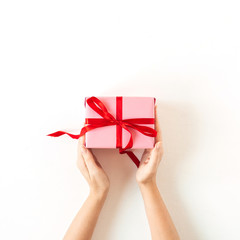 Women's hands hold pink gift box on white background. Flatlay, top view Valentine's Day holiday concept.