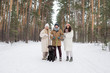 © pressmaster - Two happy girls in winterwear standing by young man with black retriever