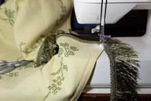 Close-up. Finishing Work On A Beautiful, Embroidered Vintage Tablecloth - Sewing On A Green Fringe With A Sewing Machine.