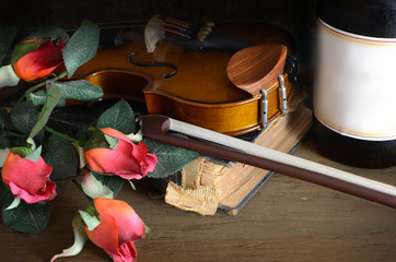 Romantic image of a violin with a glass of red wine, red roses, a botlle of wine and an old book on a rustic wooden table. Good for Valentine's Day or anniversaries. Vintage filter applied.