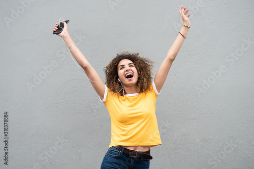 Fotografía happy young woman with arms raised holding mobile phone and listening to music b