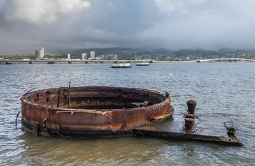 Wall Mural - Oahu, Hawaii, USA. - January 10, 2020: Pearl Harbor. Rusty part of USS Arizona sticks out of gray sea water with Honolulu skyline in back under rainy cloudy sky.