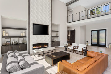 Beautiful living room interior in new luxury home. Features floor to ceiling fireplace surround, tall ceilings, built-in shelving and open concept floor plan. Shows foyer.