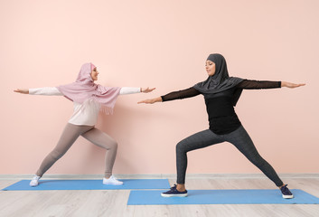 Sporty Muslim women practicing yoga near color wall