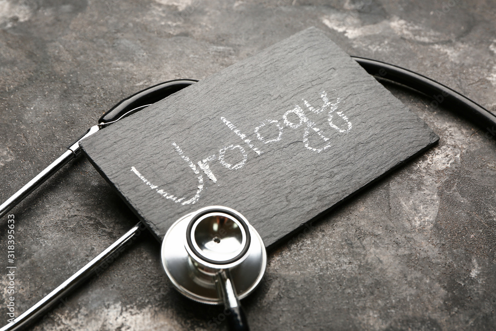 Board with text UROLOGY and stethoscope on grey background