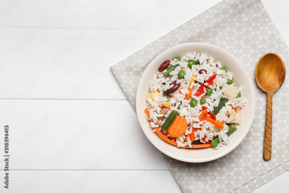 Bowl with boiled rice and vegetables on white wooden background