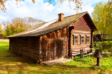 Wall Mural - Old log house darkened by time against the background of trees and cloudy sky