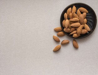 Wall Mural - Dried almonds spilled from a dark plate onto a gray background. healthy food for raw foodists and vegetarians.