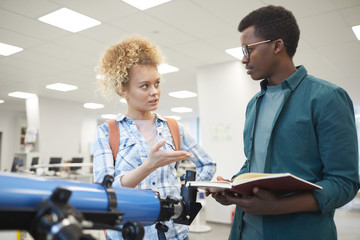 Wall Mural - Waist up portrait of two students discussing astronomy project while standing by telescope in class or college library, copy space