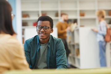 Wall Mural - Portrait of smiling African-American student discussing project with partner while sitting at table in college library, copy space