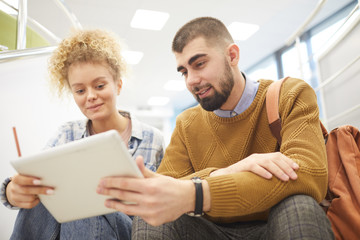 Wall Mural - Low angle portrait of student couple using digital tablet together while working on project in modern college library