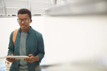 Wall Mural - Waist up portrait of young African man holding digital tablet and looking at camera while standing on staircase in college, copy space