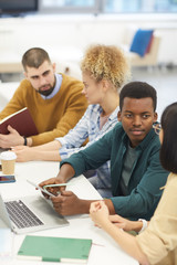 Wall Mural - High angle view at multi-ethnic group of students studying in college library, focus on African-American man talking to partner