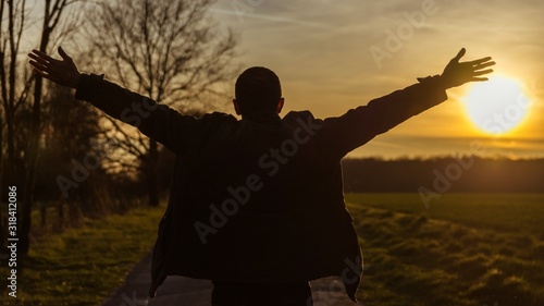 Obraz Dibond Rear View Of Silhouette Man With Arms Outstretched Standing On Field Against Sky During Sunset