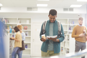 Wall Mural - Waist up portrait of African-American student reading book while standing in college library, copy space