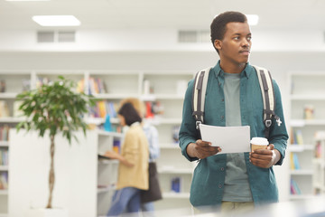 Wall Mural - Waist up portrait of African-American student holding coffee cup while standing in college library, copy space