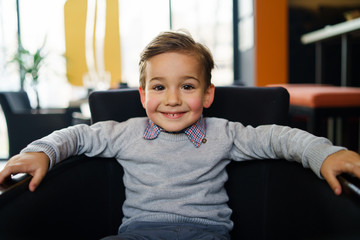 portrait of small three years old caucasian boy child sitting in the chair looking to the camera smi