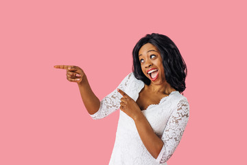 Wall Mural - Portrait of fun young woman in white lace dress pointing to side with an open mouth at copy space