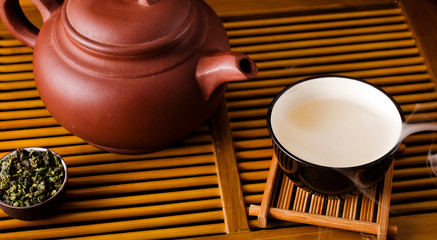 Wall Mural - Chinese tea ceremony. Ceramic tea pot and cups with the famous chinese oolong tea Tieguanyin  with vapour on a bamboo background.