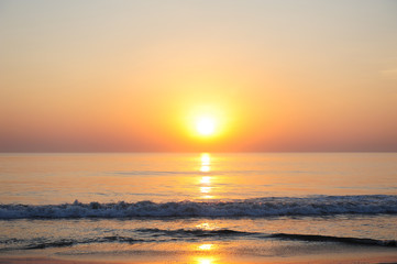 Stunning view of the sea in the rays of setting sun, reddish sunlight reflected in the water. Beautiful sunset over the ocean, deserted beach, copy space.