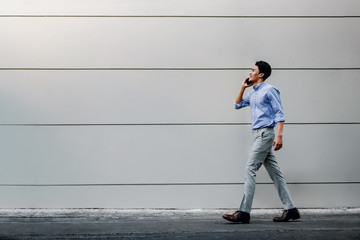 Happy Young Businessman in Casual wear Using Mobile Phone while Walking by the Urban Building Wall. Lifestyle of Modern People. Side View. Full Length