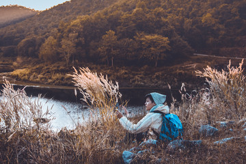 Asian young man backpackers on the grass in mountains with river enjoying their alone outdoor active lifestyle travel adventure, people hiking vacations in Thailand.