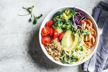 Buddha bowl salad with quinoa, avocado, broccoli, sweet potato and tahini dressing, gray background.