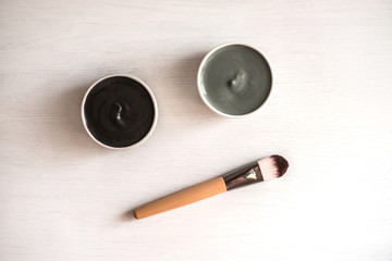 Preparing natural cosmetic black and blue facial masks in ceramic bowls on white wooden background with brush. Rustic style.