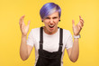 © khosrork - Portrait of aggressive hipster girl with violet dyed short hair in denim overalls quarreling with raised hands, screaming in anger with mad and furious face. isolated on yellow background, studio shot