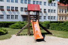 Old Retro Vintage Outdoor Wooden Public Playground Equipment With Climbing Steps And Dilapidated Plastic Slide Surrounded With Gravel Grass And Dense Hedge In Public Park
