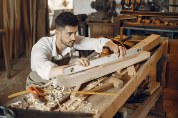 Wall Mural - Man working with a wood. Carpenter in a white shirt. Worker measures a board