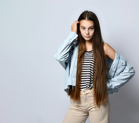 Teenage girl in striped t-shirt, denim jacket and pants. She looking at you, posing isolated on white studio background. Close up