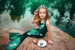 © Вероника Преображенс - A little girl with white hair with a mermaid tail and shells is sitting on the shore. A little mermaid sits on a large stone by the pond.