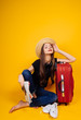 with vouchers and guides in her hands, the girl in the hat leaned on a suitcase. background yellow