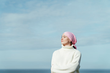 portrait of young woman with cancer and crossed arms with closed eyes and sky on background