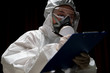 © marchsirawit - Woman wearing gloves with biohazard chemical protective suit and mask. is writing report on paper.