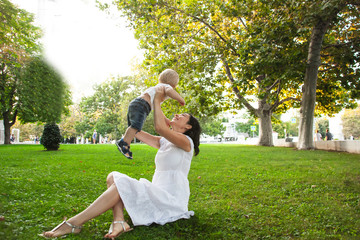 Wall Mural - young woman sit on the grass on the nature park and holding the baby. mother have fun with toddler.