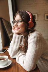 Poster - Image of young woman wearing headphones listening to music in cafe