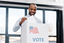 Happy African American Man Voting And Putting Ballot In Box With Flag Of America