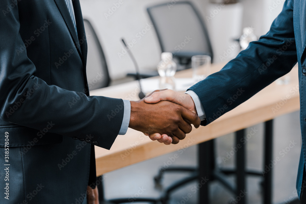 cropped view of businessman shaking hands with african american diplomat - obrazy, fototapety, plakaty 