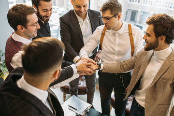 Wall Mural - young caucasian leaders joined hands in one, wearing formal suits, successful cooperation of business people. success depends on cohesion and teamwork