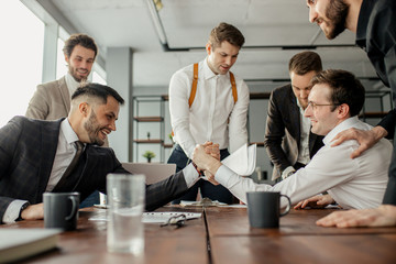 Wall Mural - positive coworking business men in tuxedo, cheerfully playing arm wrestling after working day in office