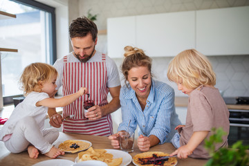 Wall Mural - Young family with two small children indoors in kitchen, eating pancakes.