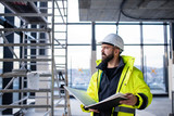 Fototapeta  - Man engineer standing on construction site, holding blueprints.