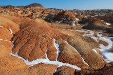 Eroded Desert Landscape With Clay Layers And Snow