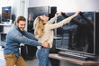 angry boyfriend pulling girlfriend with tv in home appliance store