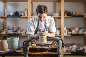 Potter working on a Potter's wheel making a vase. Young woman forming the clay with hands creating jug in a workshop.