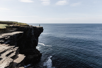 Man Standing On Cliff By Sea Against Sky